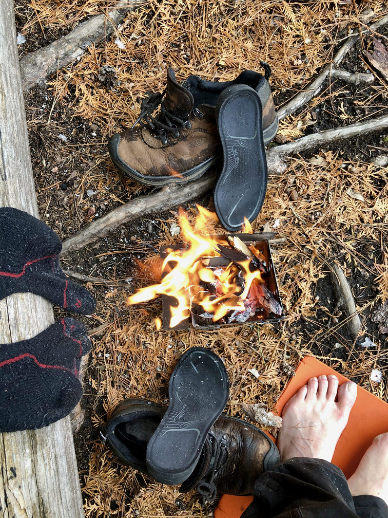 Des pieds, chaussettes et chaussures qui sèchent autour d’un réchaud à bois